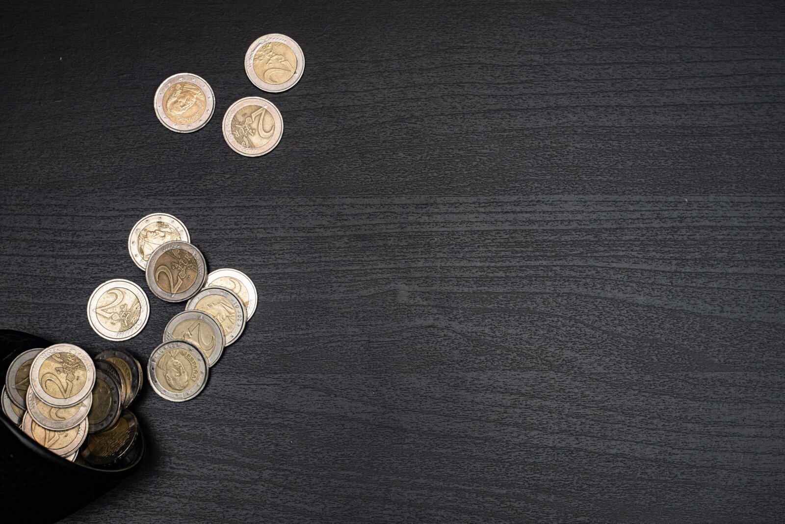 Euro coins scattered from a small purse onto a dark surface.