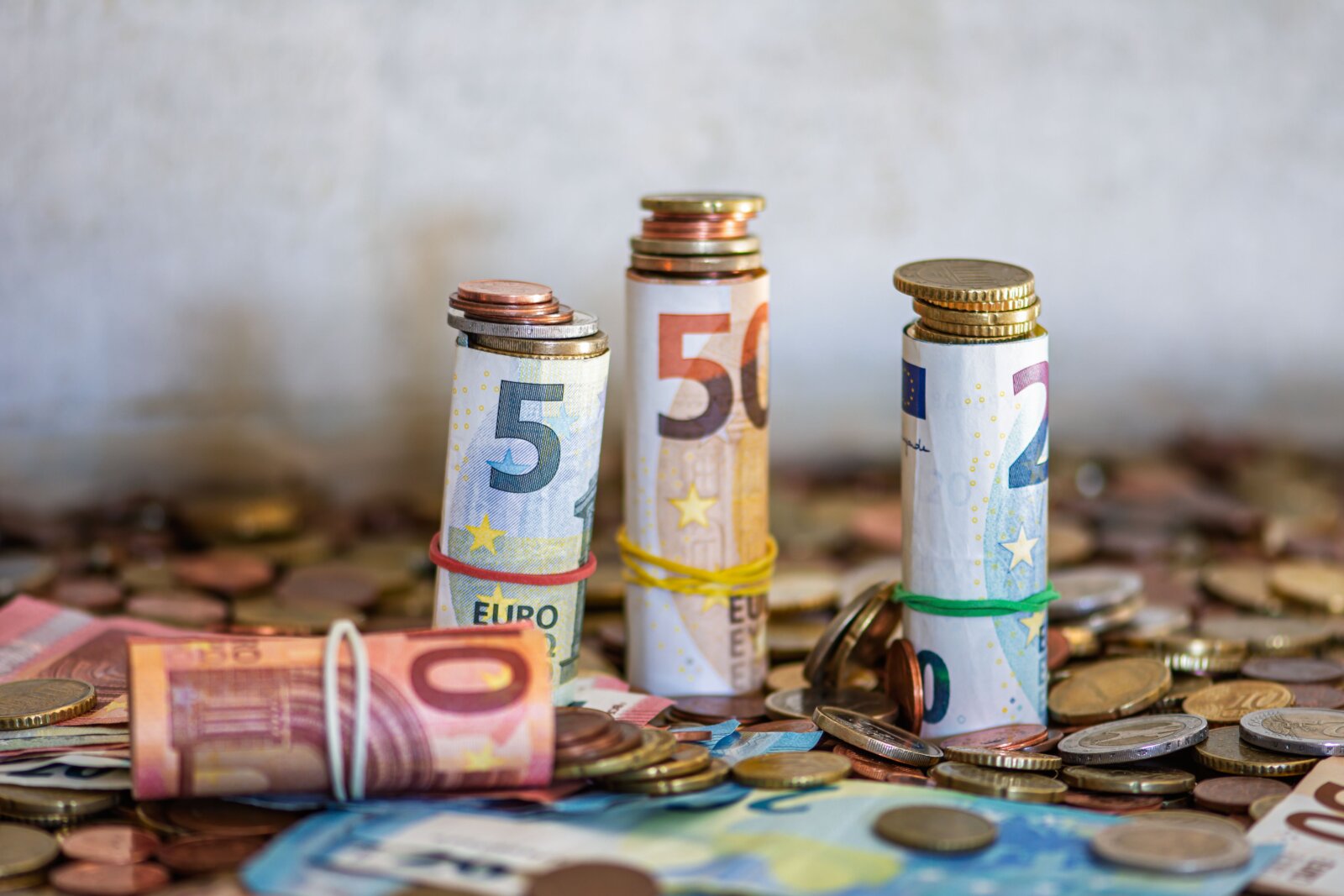 Rolled euro banknotes standing among loose coins on a table.