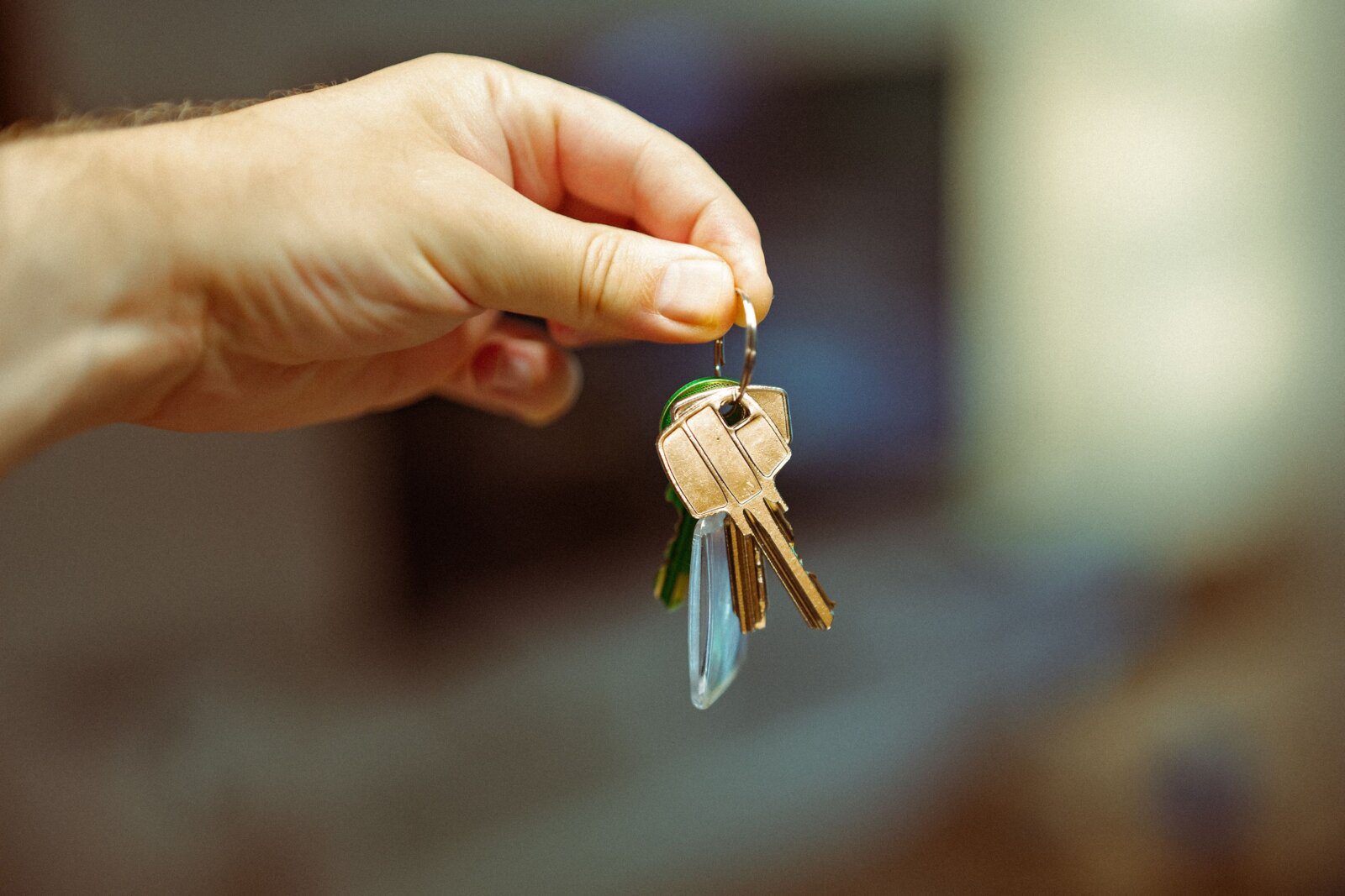 A hand holding a keyring with several house keys against a blurred interior.