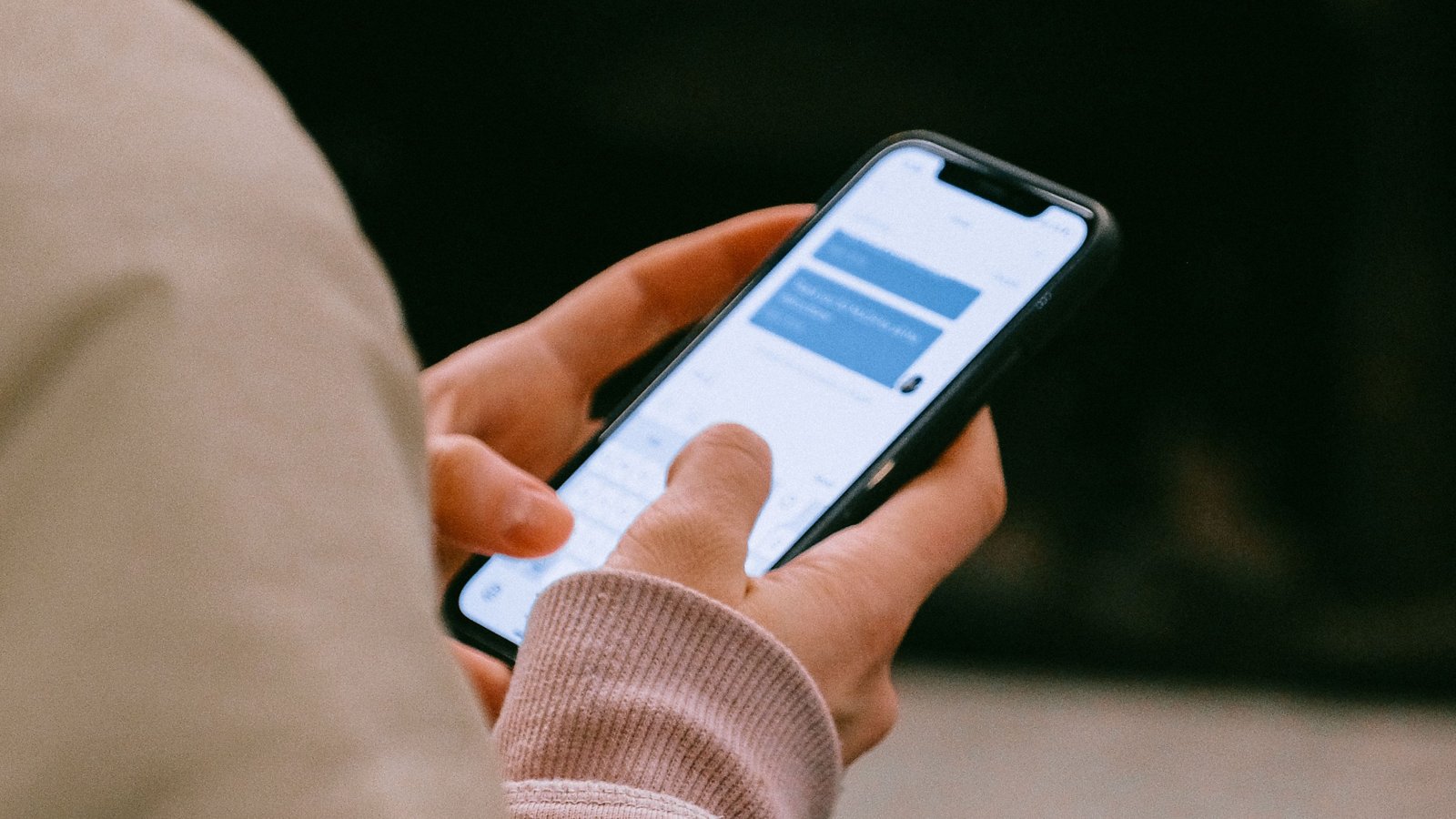 Hands using a smartphone with blue message bubbles on its screen.