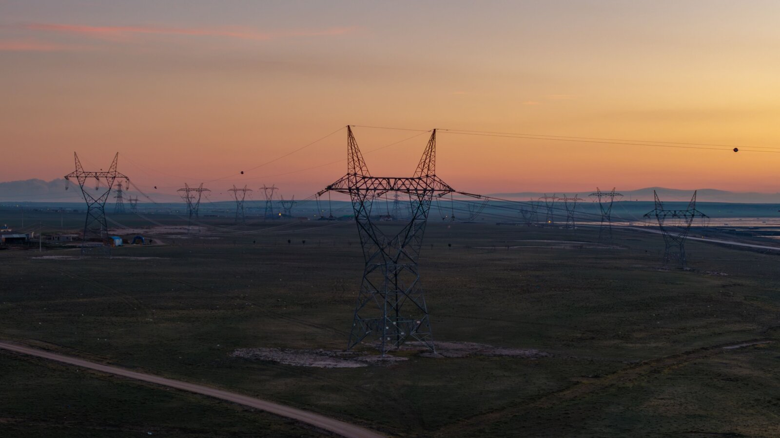 Electricity transmission pylons crossing open land beneath a sunset sky.